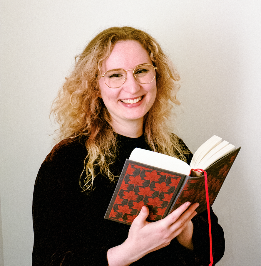 A photo of author Sasha Vey, a smiling blonde woman with glasses, holding a book